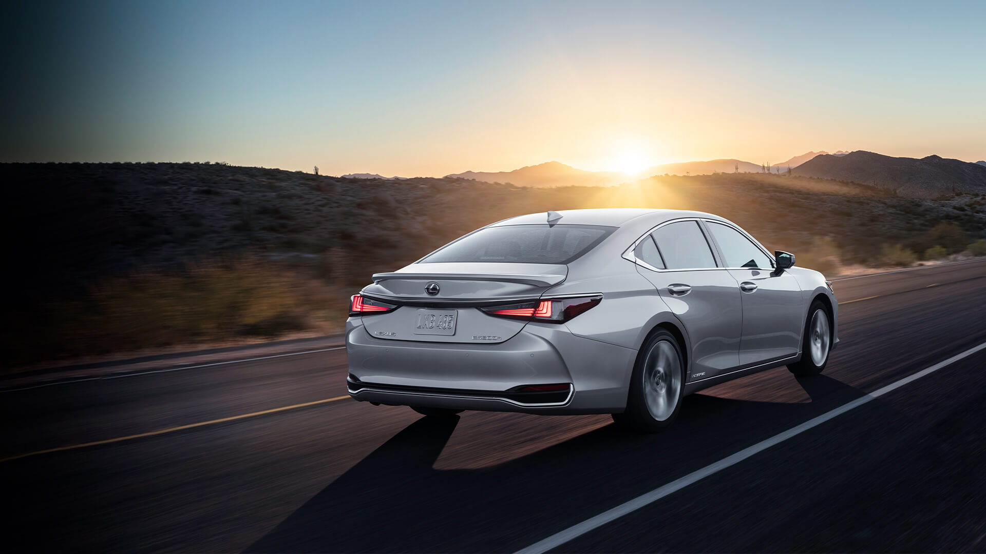 Silver Lexus ES on an open road against a sunset.