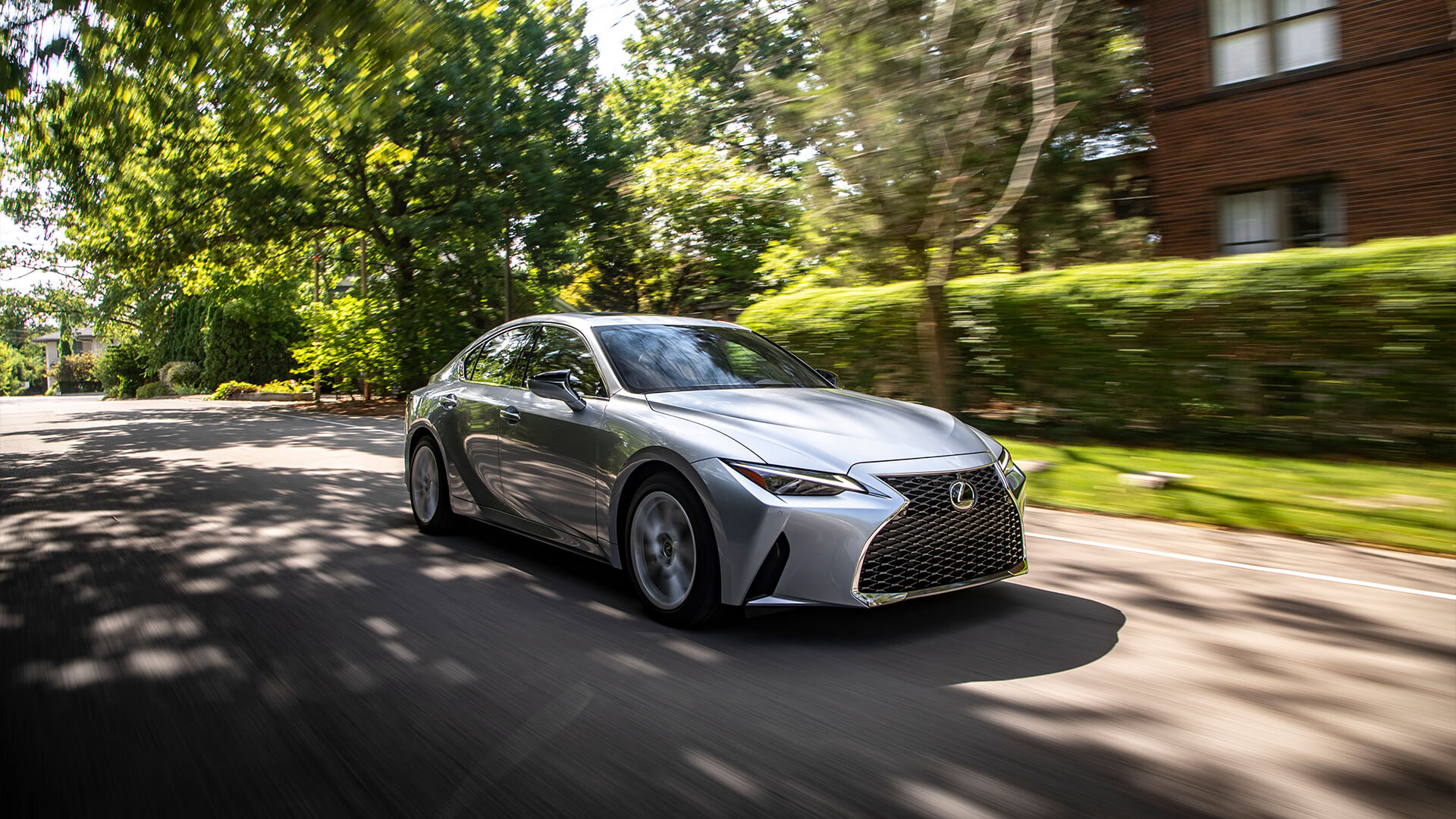 Silver Lexus IS being driven on a road with trees on both sides.