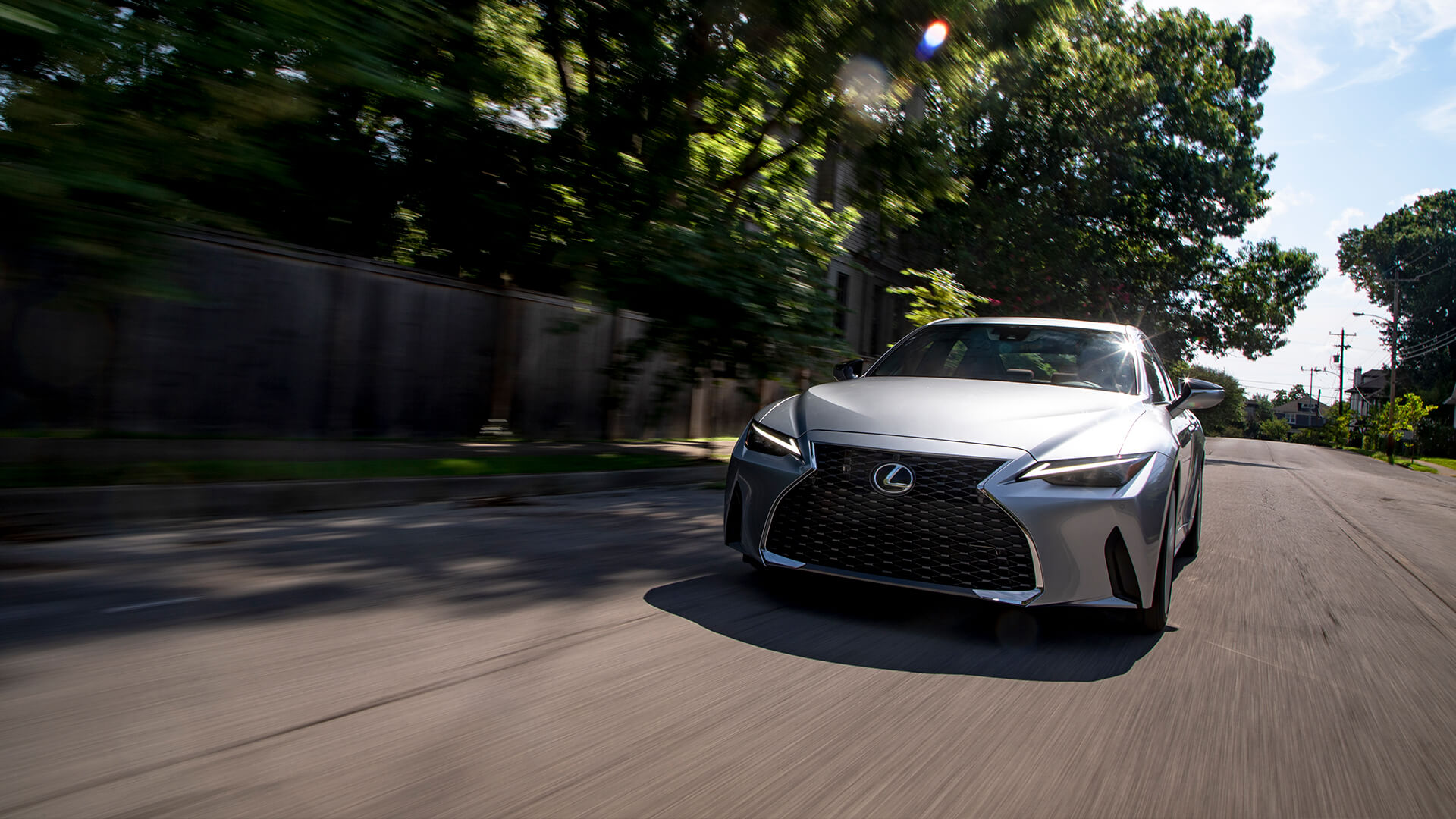 Silver Lexus IS being driven on a road with trees on both sides.