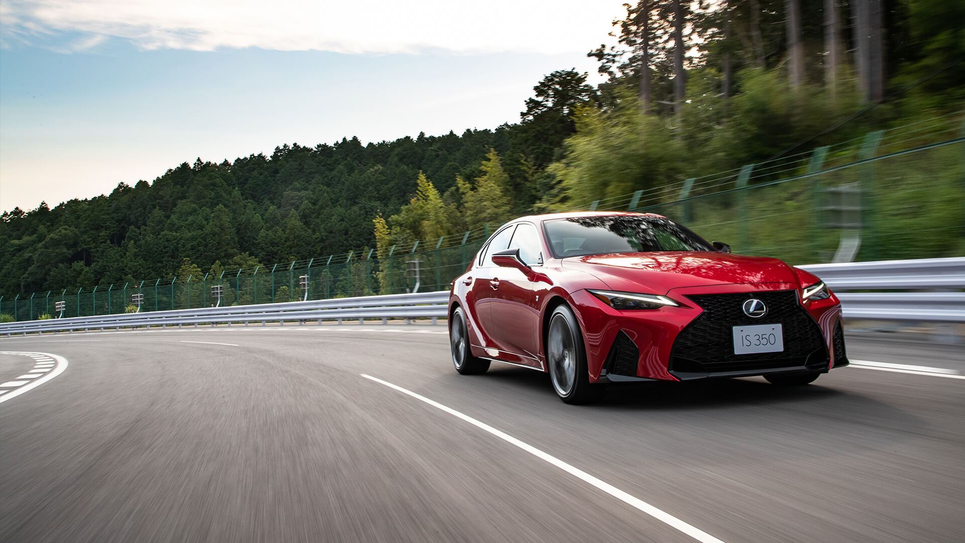Red Lexus IS being driven on the road.