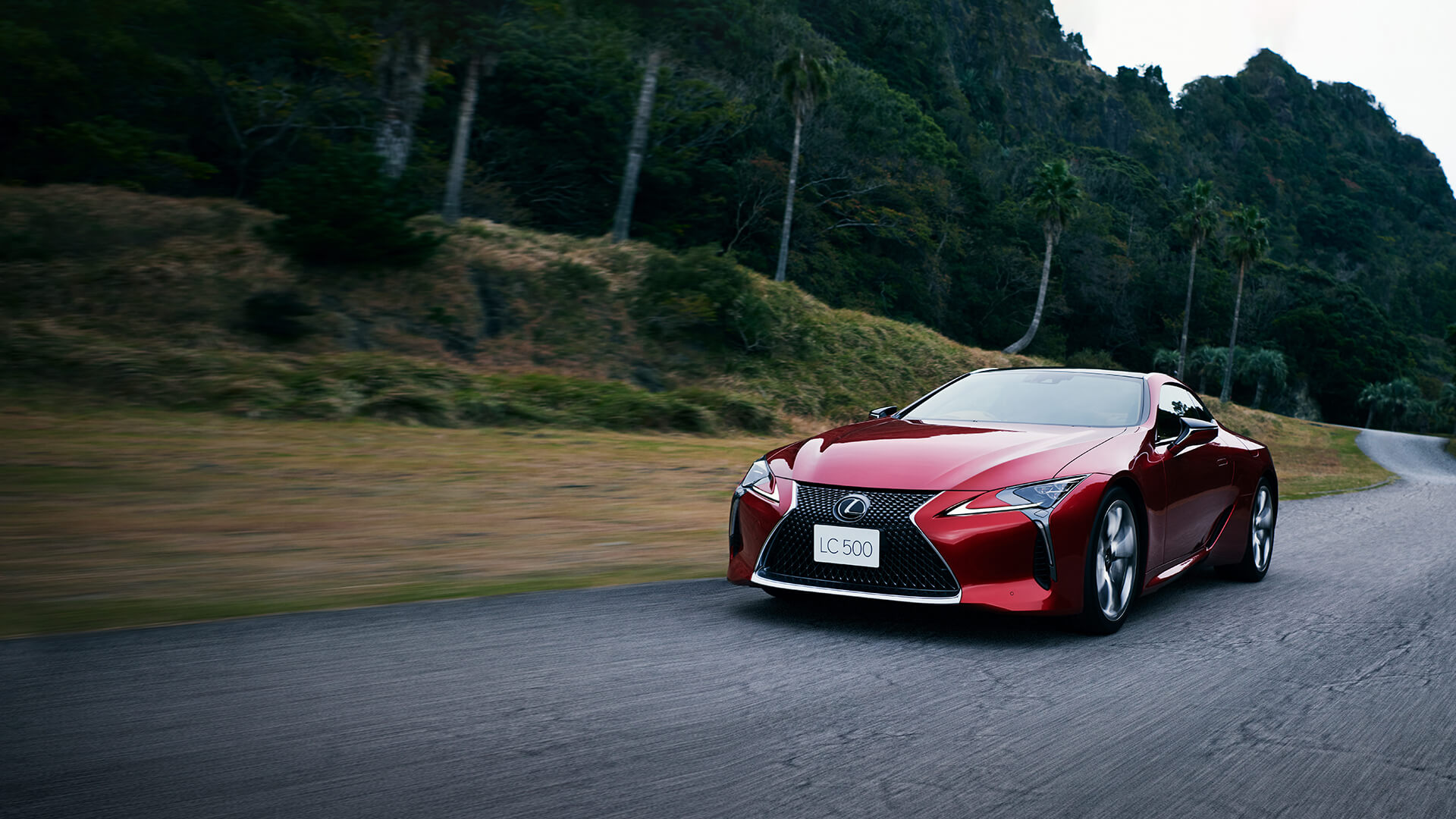 Red Lexus LC 500 being driven on the road in a forested area.